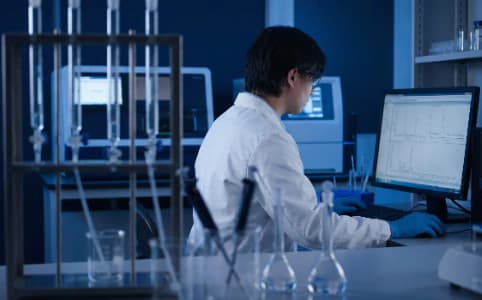 A laboratory researcher reviewing analytical data at a computer workstation in a blue-lit lab
